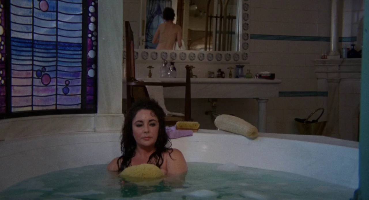 Secret Ceremony (1968) movie still: medium — A vintage-style bathroom features a circular tub and a tall, decorative stained glass window. A woman…