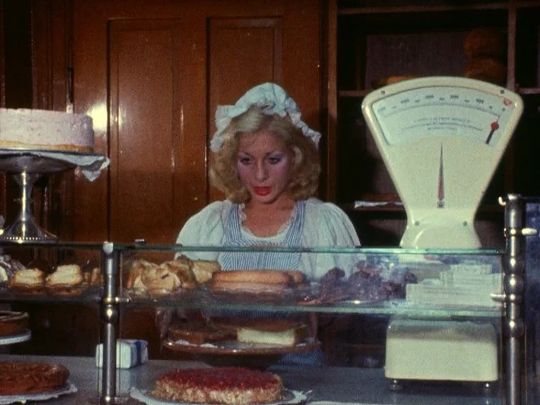 Der Bomberpilot (1970) movie still: medium — A vintage bakery features a glass display case filled with assorted cakes and tarts. A woman in a…