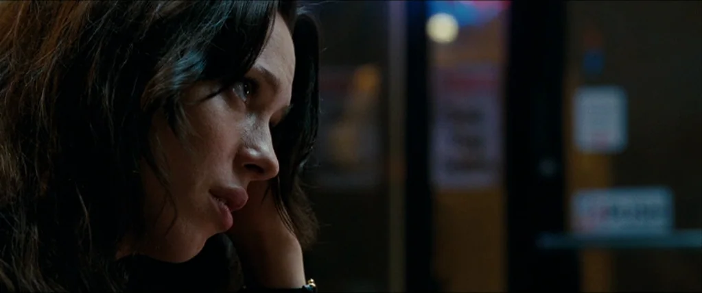 The Town (2010) movie still: closeup — A dark diner booth interior with blurred lights in the background. A woman leans her head on her hand while…