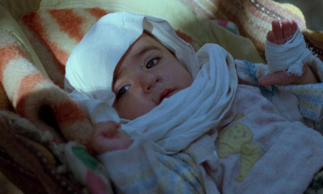 Life, and Nothing More (1992) movie still: closeup — An infant lies in a soft fabric-lined crib in a dimly lit space. The child has a white bandage…