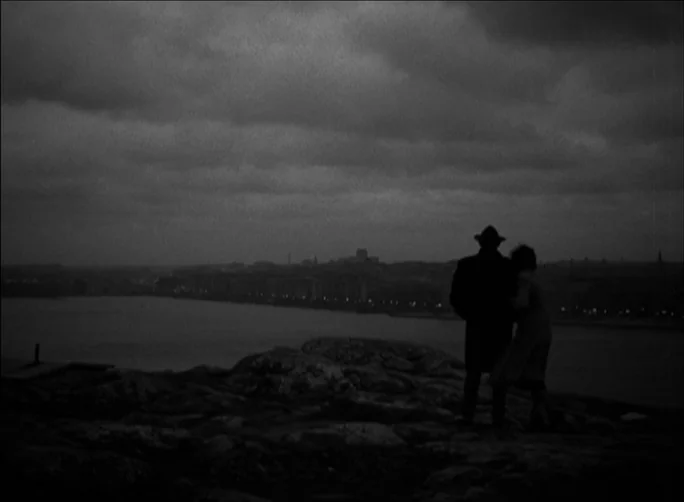 Summer with Monika (1953) movie still: wide — A rocky vantage point overlooking a dark body of water under a cloudy night sky. A man and a woman…