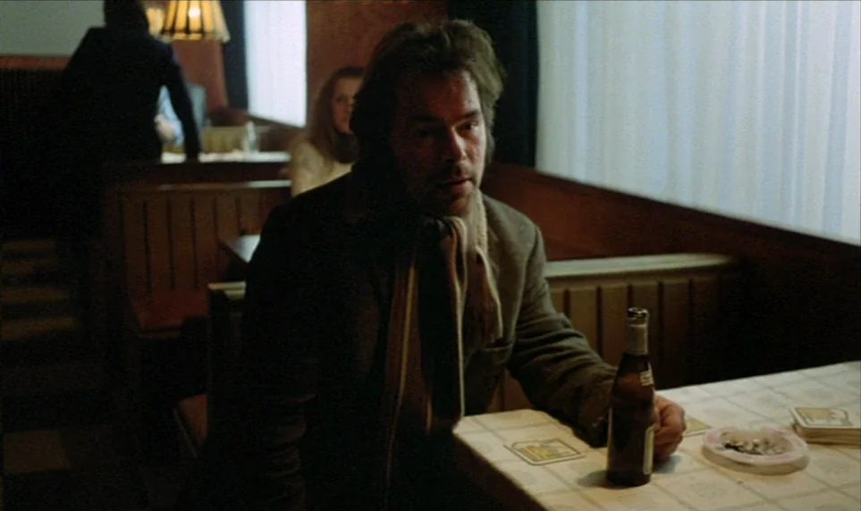 Stroszek (1977) movie still: medium — A dimly lit diner booth at night features wood-paneled walls and a white tablecloth. A man sits alone at the…