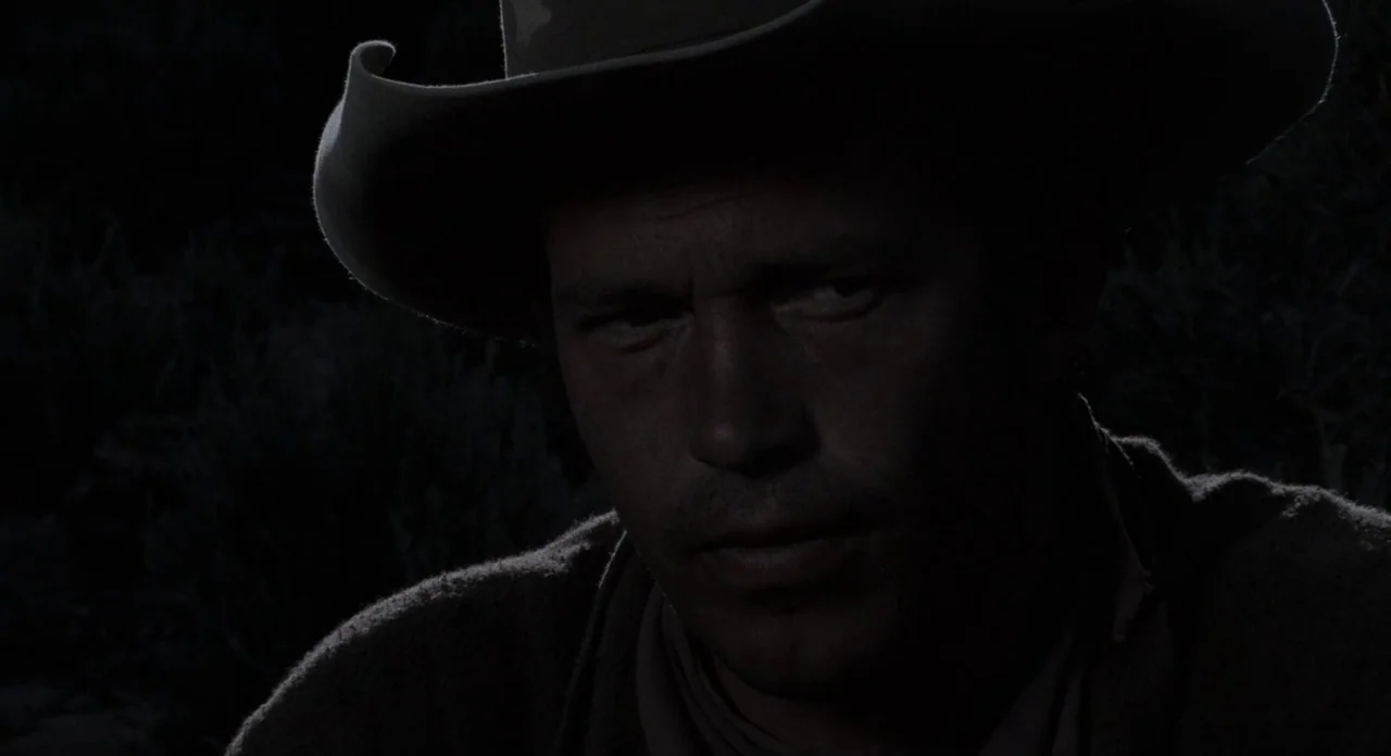 The Shooting (1966) movie still: closeup — A man wears a wide-brimmed hat in a dark, outdoor setting at night. He stares ahead into the shadows…