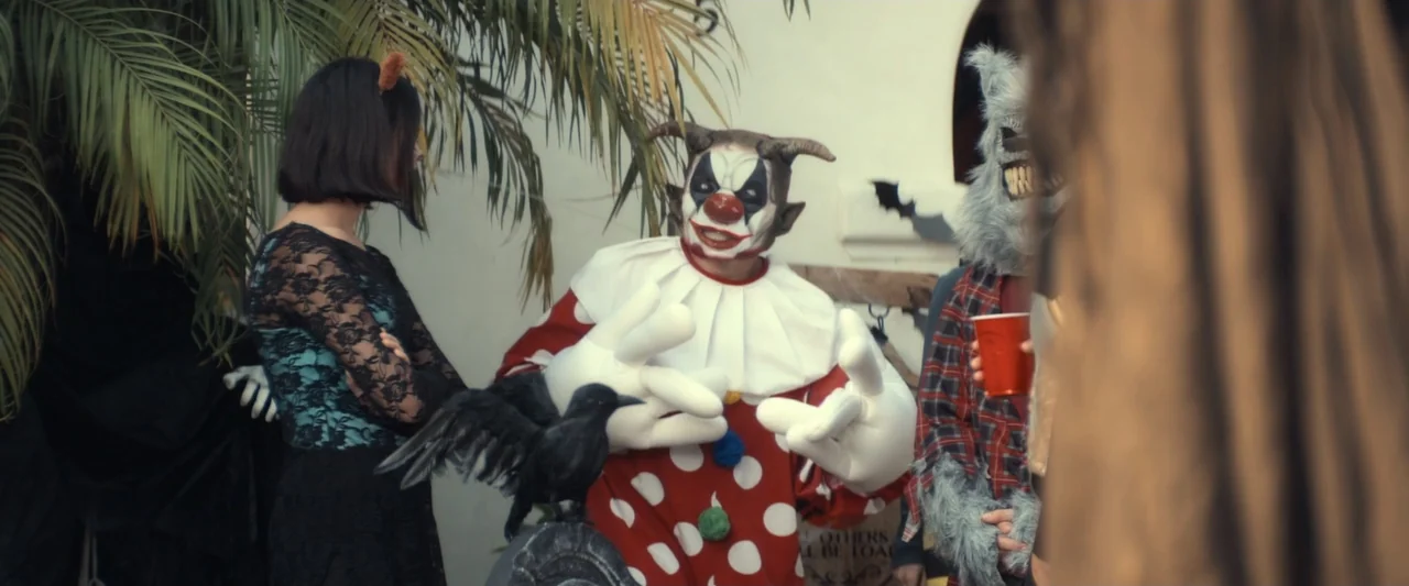 I Love America (2022) movie still: medium — A residential patio decorated for a party features costumed people standing near palm trees. A person…