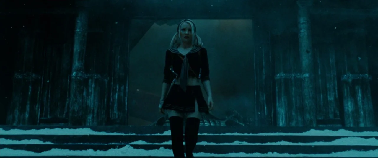 Sucker Punch (2011) movie still: fullbody — A dark stone structure stands in the snow under deep blue night illumination. A young woman walks…