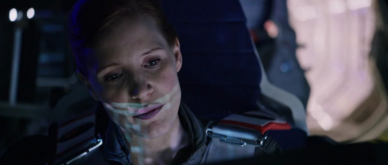 The Martian (2015) movie still: closeup — A dimly lit spacecraft cockpit contains complex control panels and flight hardware. A woman looks downward…