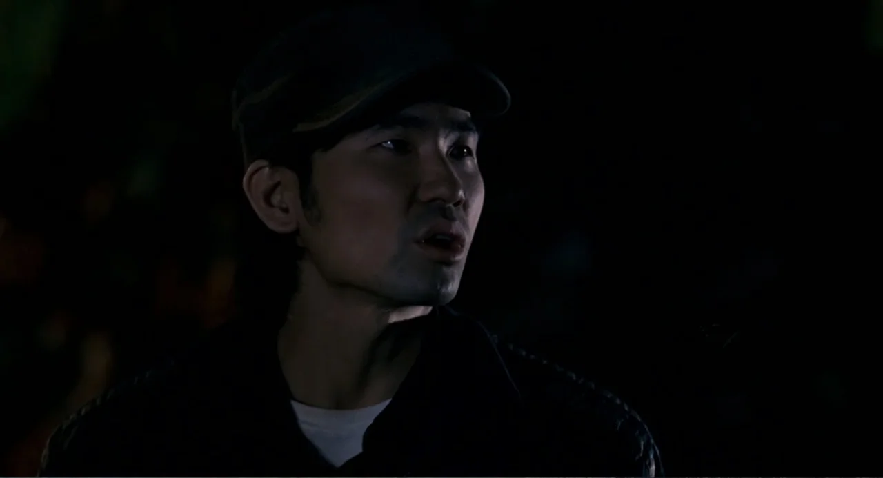 Management (2009) movie still: closeup — A man stands in an dark outdoor environment at night with low lighting. He is looking off to the side with…