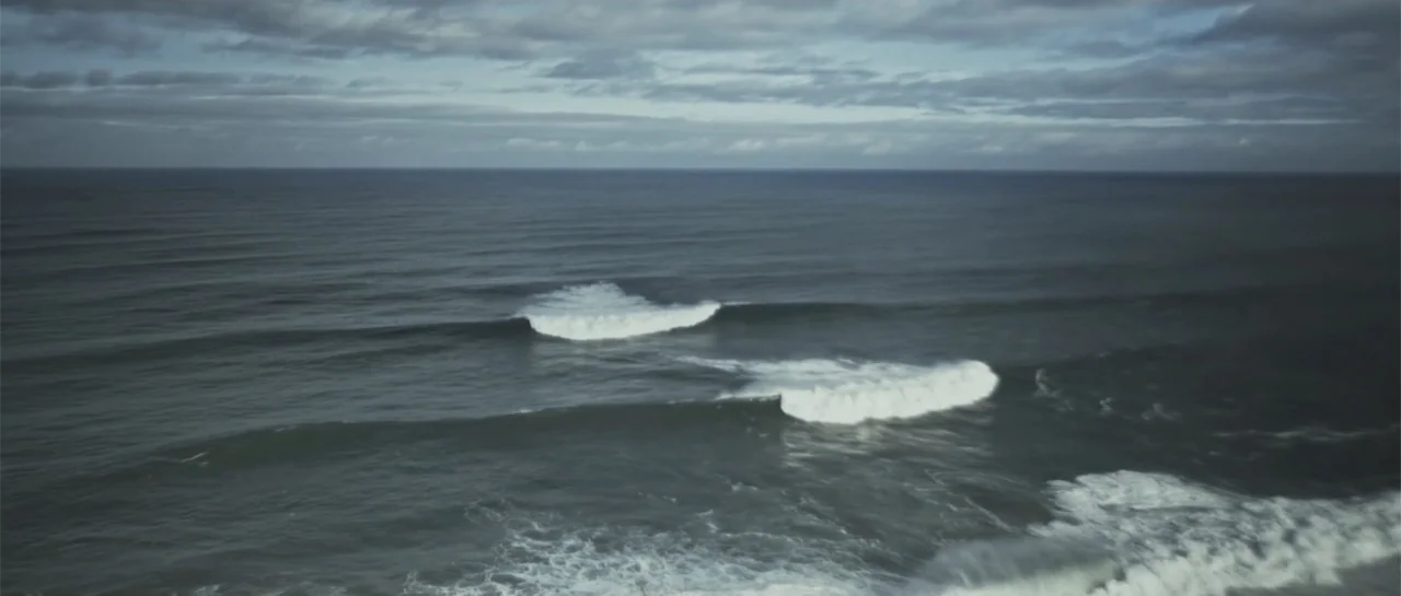 Taking Back the Waves (2017) movie still: establishing — A vast expanse of ocean under a cloudy sky with white-capped waves. Two distinct sets of…