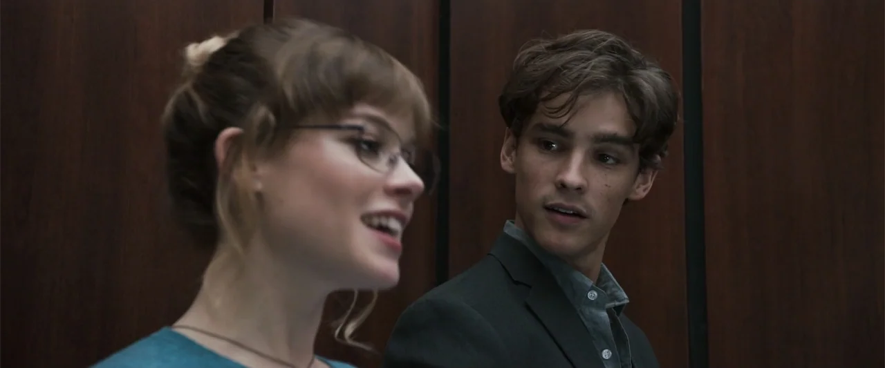 Office Uprising (2018) movie still: medium — An elevator interior features dark wood paneled walls as a backdrop for the subjects. A young man and…