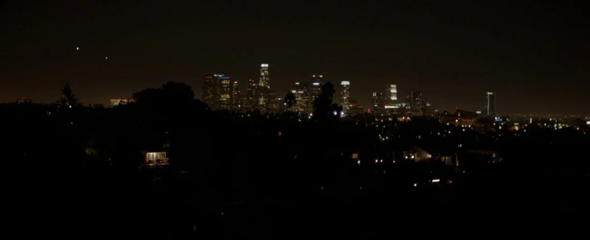 Cheap Thrills (2013) movie still: establishing — A panoramic night view captures a distant skyline silhouetted against a vast, dark sky. Trees and…