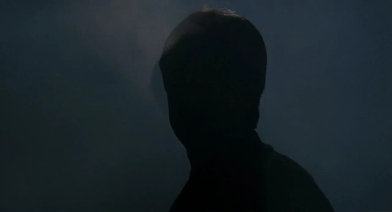 Dangerously Close (1986) movie still: closeup — A dark, indistinct space is filled with faint haze or smoke. A man in silhouette stands with his…