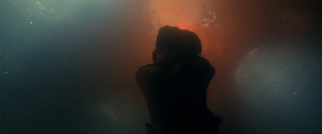Madame Web (2024) movie still: medium — A dark, murky environment with light diffusing through the water around a subject. A person floats in…
