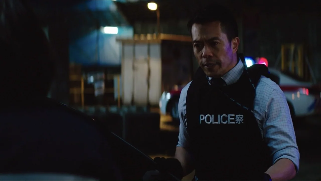Skyscraper (2018) movie still: medium — An exterior nighttime scene set in a dim urban area with a patrol car parked nearby. A male police officer…