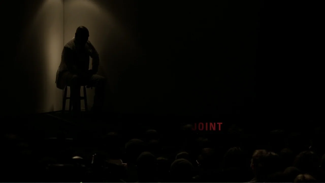Mike Tyson: Undisputed Truth (2013) movie still: wide — A man sits alone on a stool on a dark theater stage. The word JOINT is displayed in red…