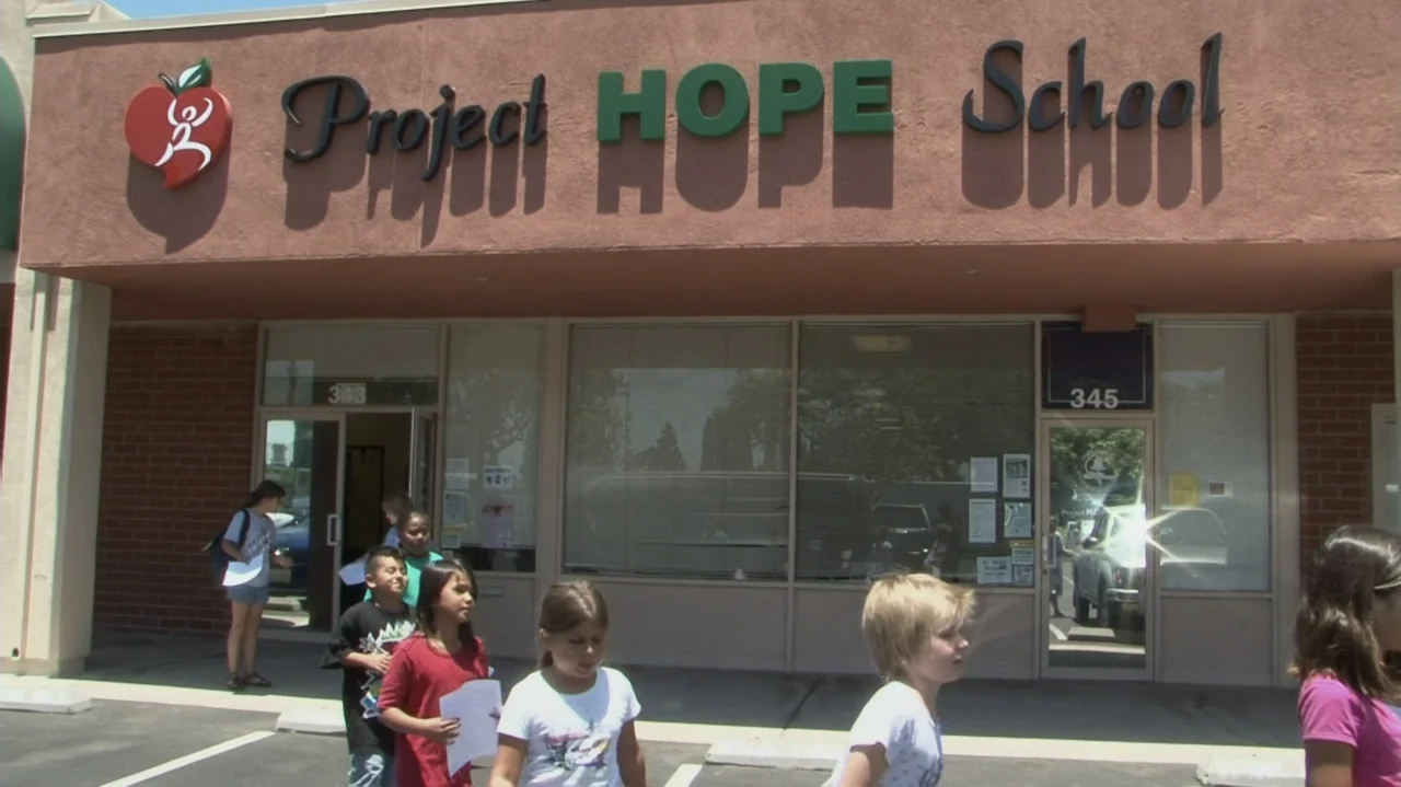 Homeless: The Motel Kids of Orange County (2010) movie still: medium — An exterior view of a school storefront with a stucco wall and glass windows.…