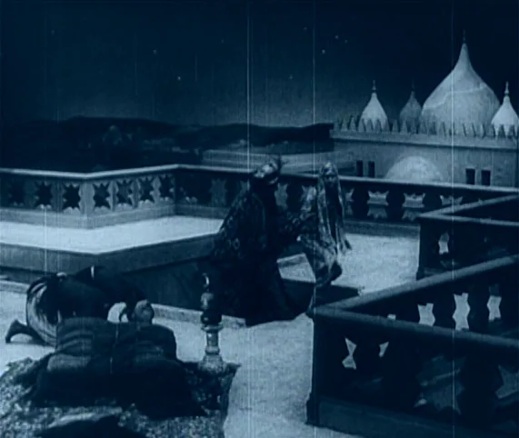 Destiny (1921) movie still: wide — An ornate terrace rooftop at night overlooks a distant building with multiple domes. Three people move across the…