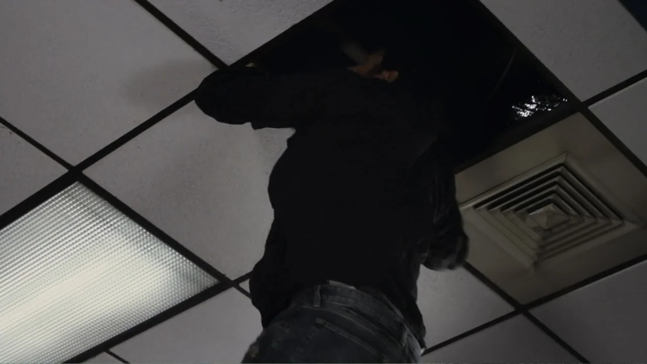 Flypaper (1999) movie still: medium — A drop ceiling in an office space with a removed square panel. A man reaches into the dark opening above the…