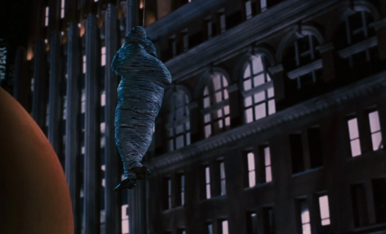 James and the Giant Peach (1996) movie still: medium — A dark city block features a towering facade with many illuminated rectangular windows. A…