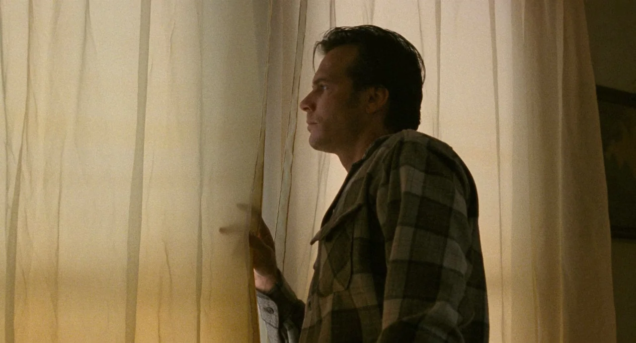 One False Move (1991) movie still: medium — A man in a checked shirt stands in a room behind white curtains. He looks past the fabric toward an…