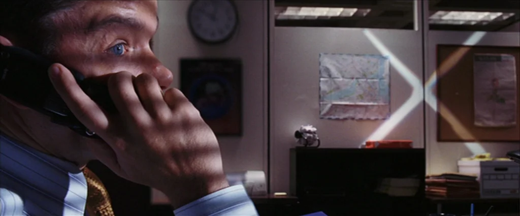 The Departed (2006) movie still: closeup — An office cubicle features a wall-mounted clock and a map pinned to the partition. A man in a dress shirt…
