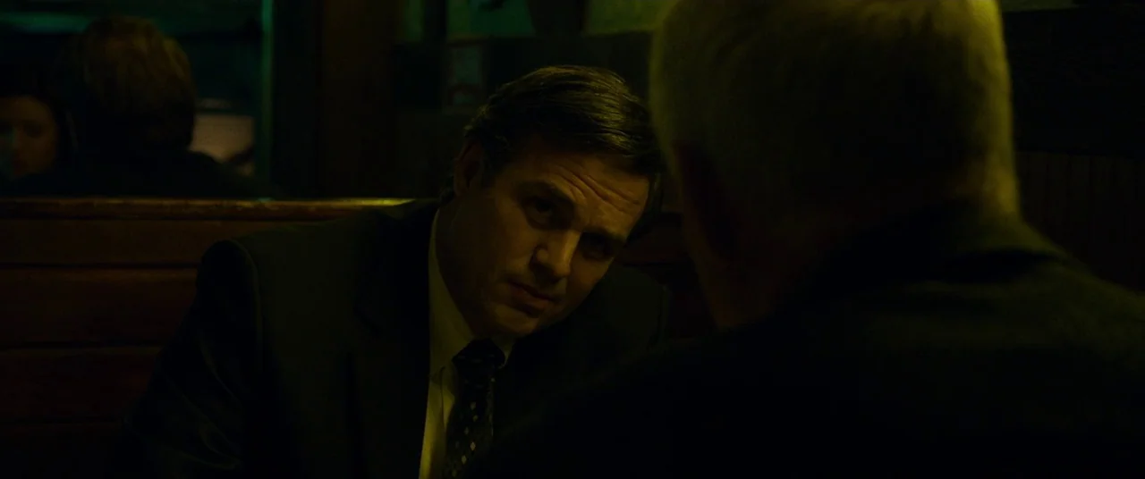 Dark Waters (2019) movie still: medium — A dimly lit diner booth at night with wood-paneled walls in the background. A man in a dark suit sits…