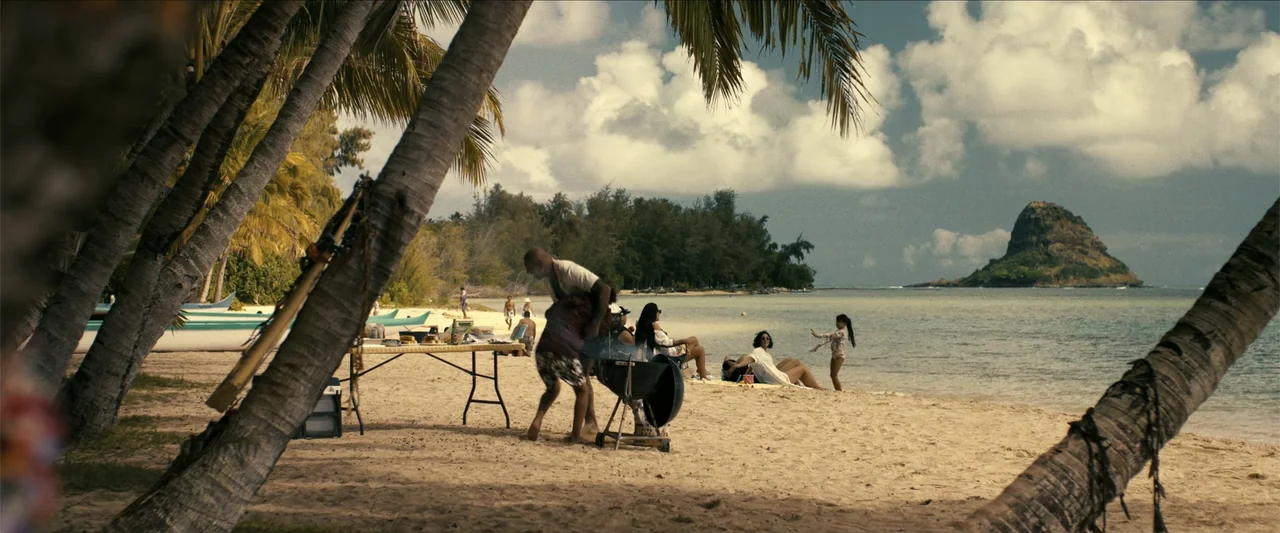 The Wrecking Crew (2026) movie still: wide — A sunny tropical beach featuring palm trees and a small island in the distance. Several people…