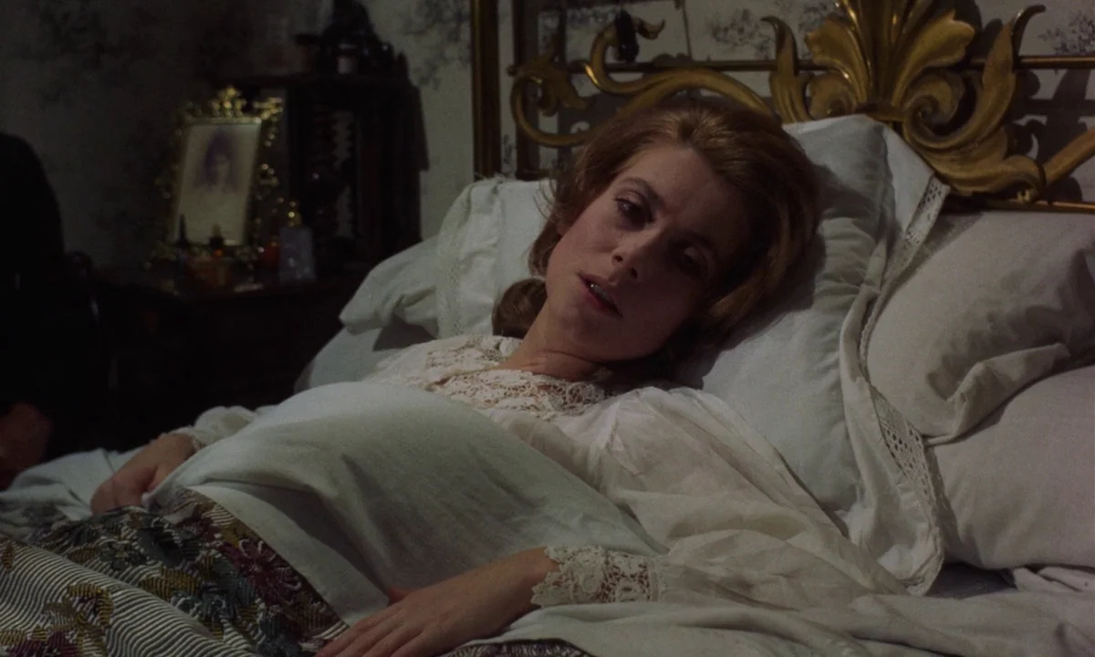 Tristana (1970) movie still: medium — A dimly lit room features a decorative gilded bed frame and floral wallpaper. A woman in a white nightgown…