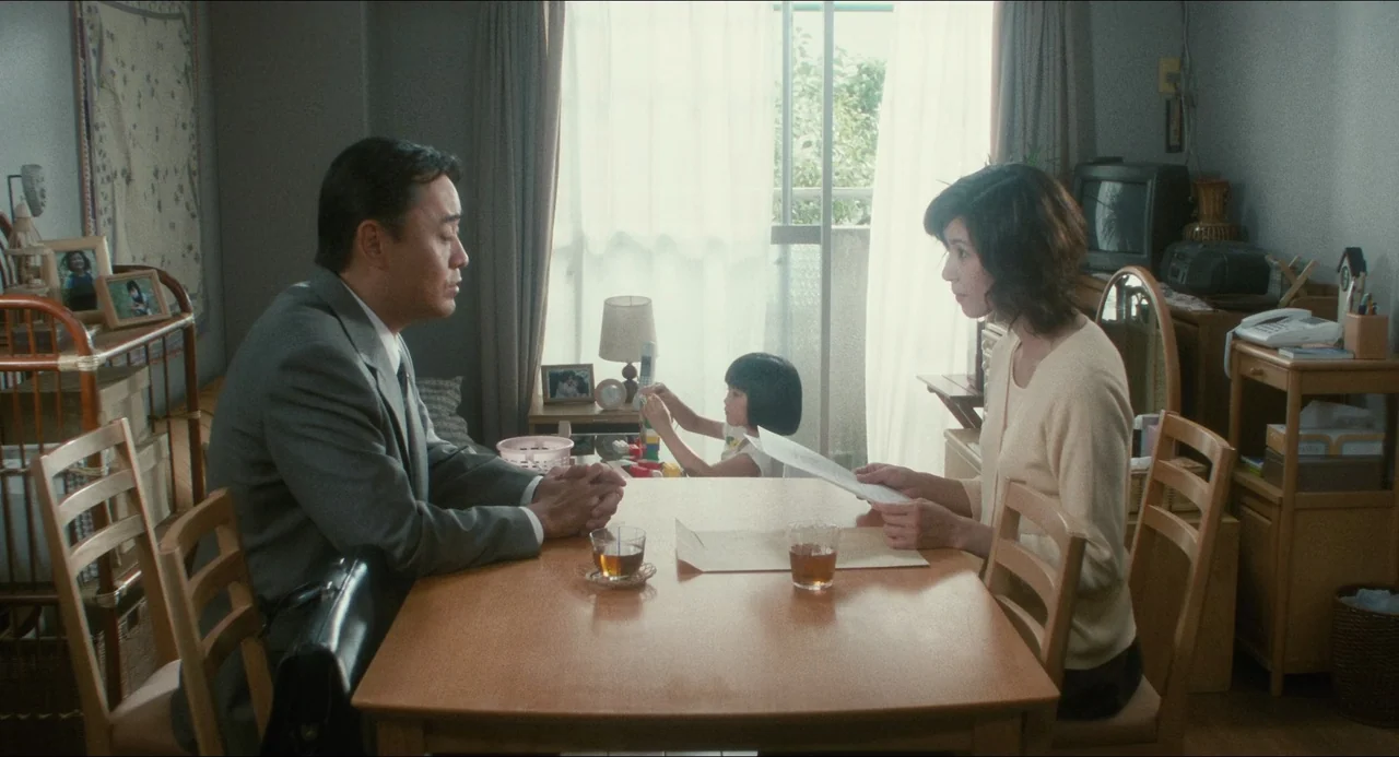 Dark Water (2002) movie still: medium — A residential dining room features light wooden furniture and a large window with sheer curtains. A man in a…