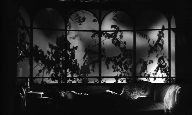 The Girl Who Knew Too Much (1963) movie still: wide — An interior space features large arched windows looking out onto silhouetted branches. The…