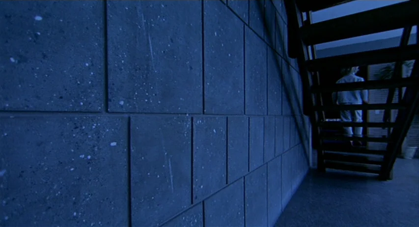 The Fifth Cord (1971) movie still: wide — A modern stairwell features walls composed of large, speckled grey modular panels. A lone person ascends…