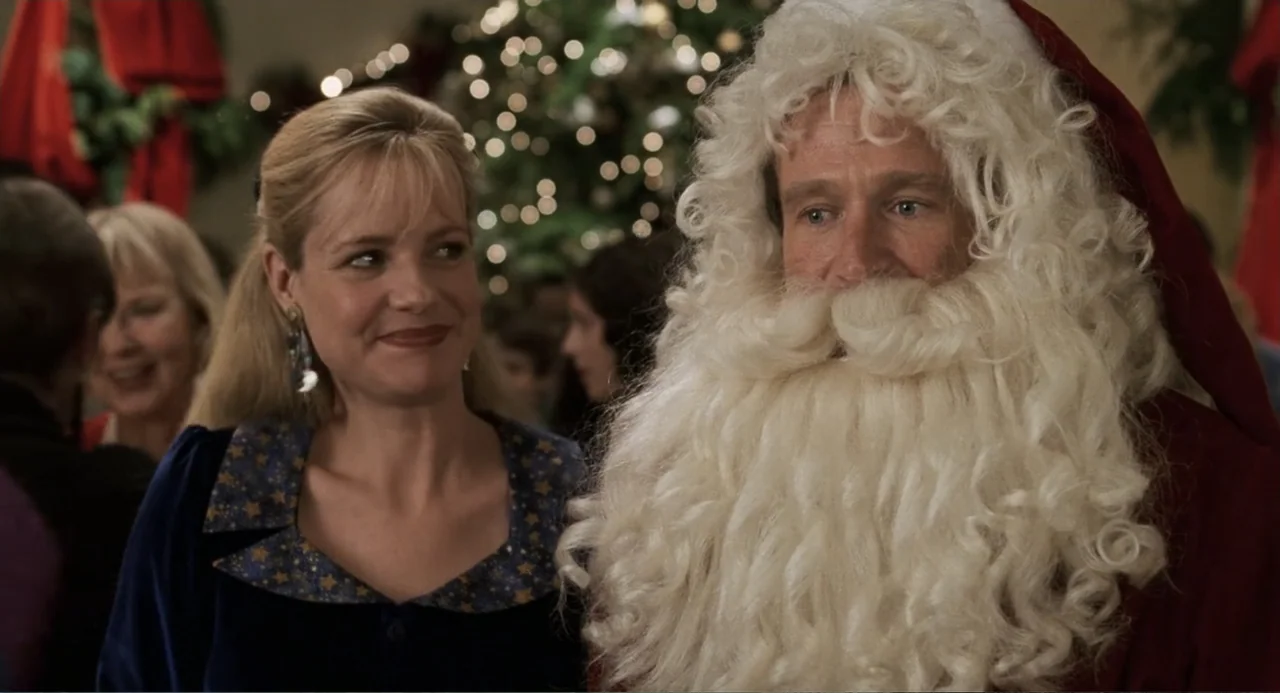 Jumanji (1995) movie still: medium — A festive indoor gathering features a decorated Christmas tree in the blurred background. A woman looks toward…