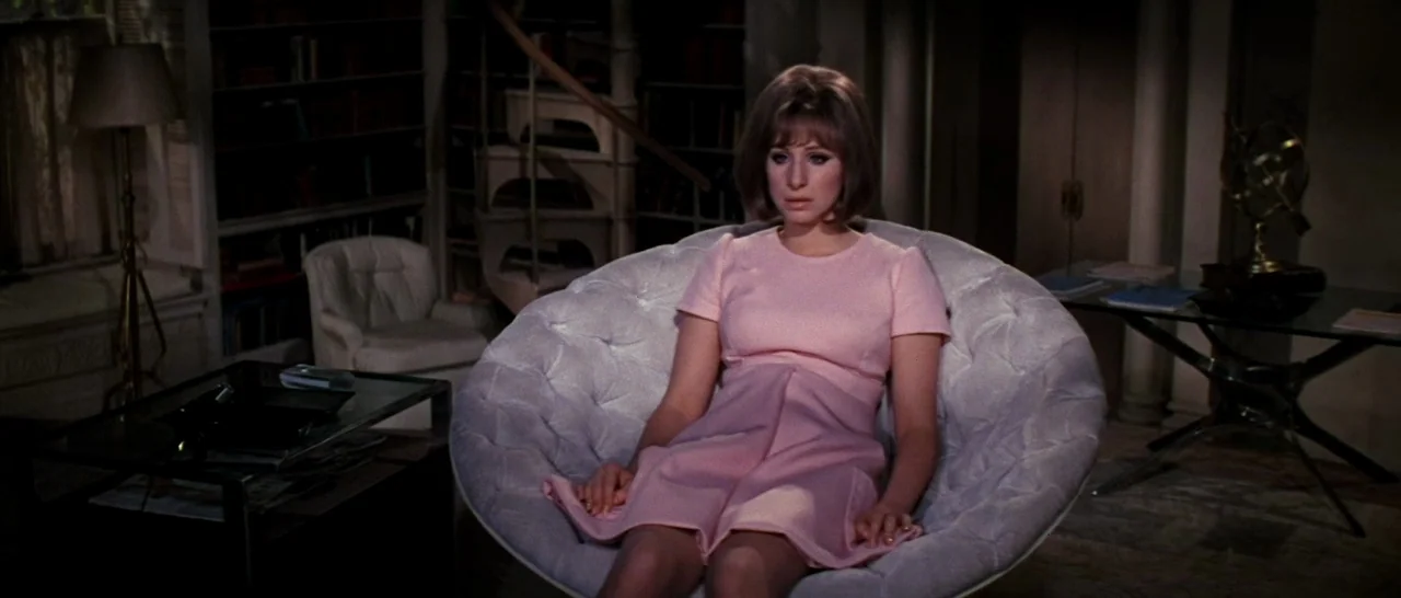On A Clear Day You Can See Forever (1970) movie still: medium — A dimly lit room features a spiral staircase and bookshelves in the background. A…