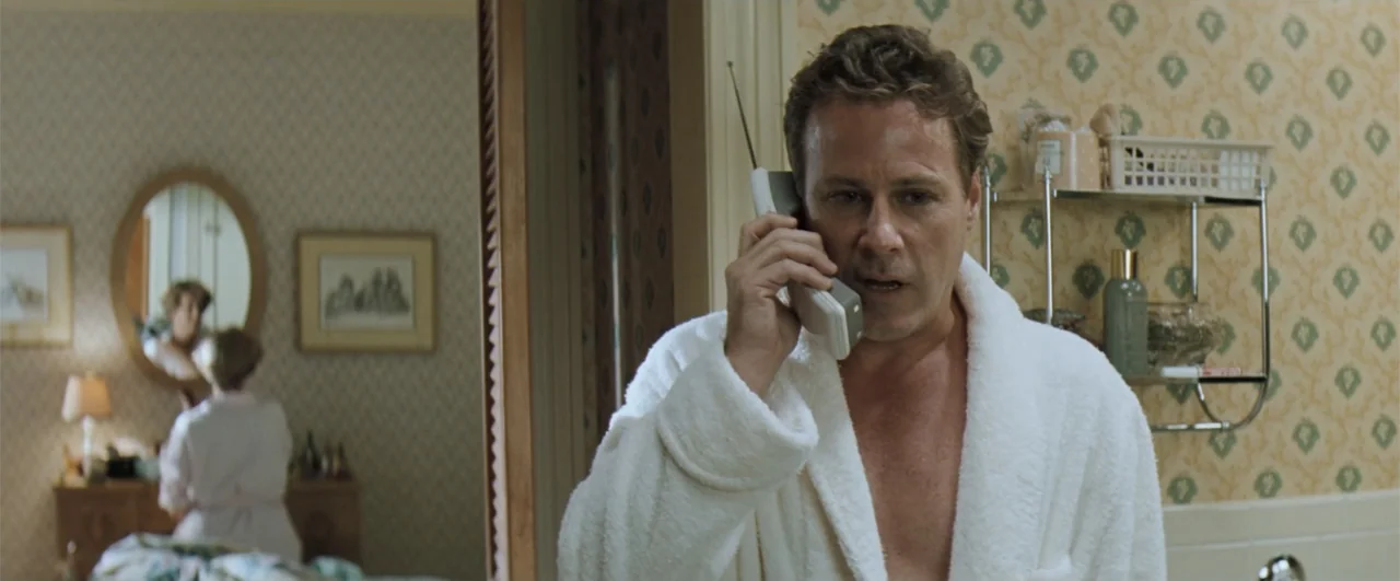 The Pelican Brief (1993) movie still: medium — A residential bathroom with patterned wallpaper and an adjacent bedroom visible through the doorway.…