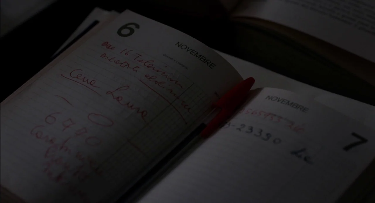 Pasolini (2014) movie still: closeup — An open diary page shows handwritten Italian notes in red ink for November sixth. A red plastic pen rests…
