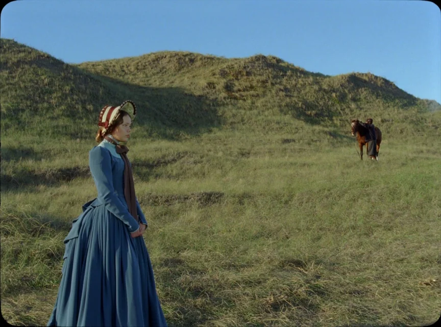 Jauja (2014) movie still: fullbody — A grassy hill under a clear blue sky serves as a backdrop. A woman in a blue dress stands in the foreground…