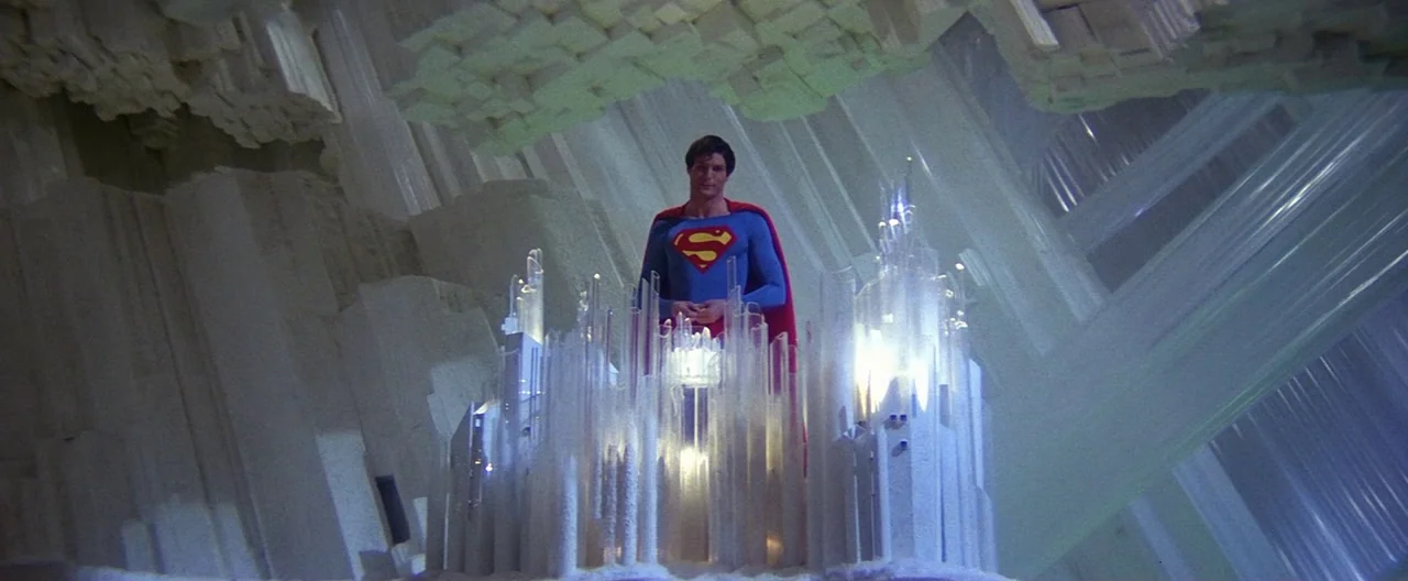Superman (1978) movie still: wide — A vast cavern constructed of sharp, jagged white translucent crystal pillars. A man in a blue hero suit stands…