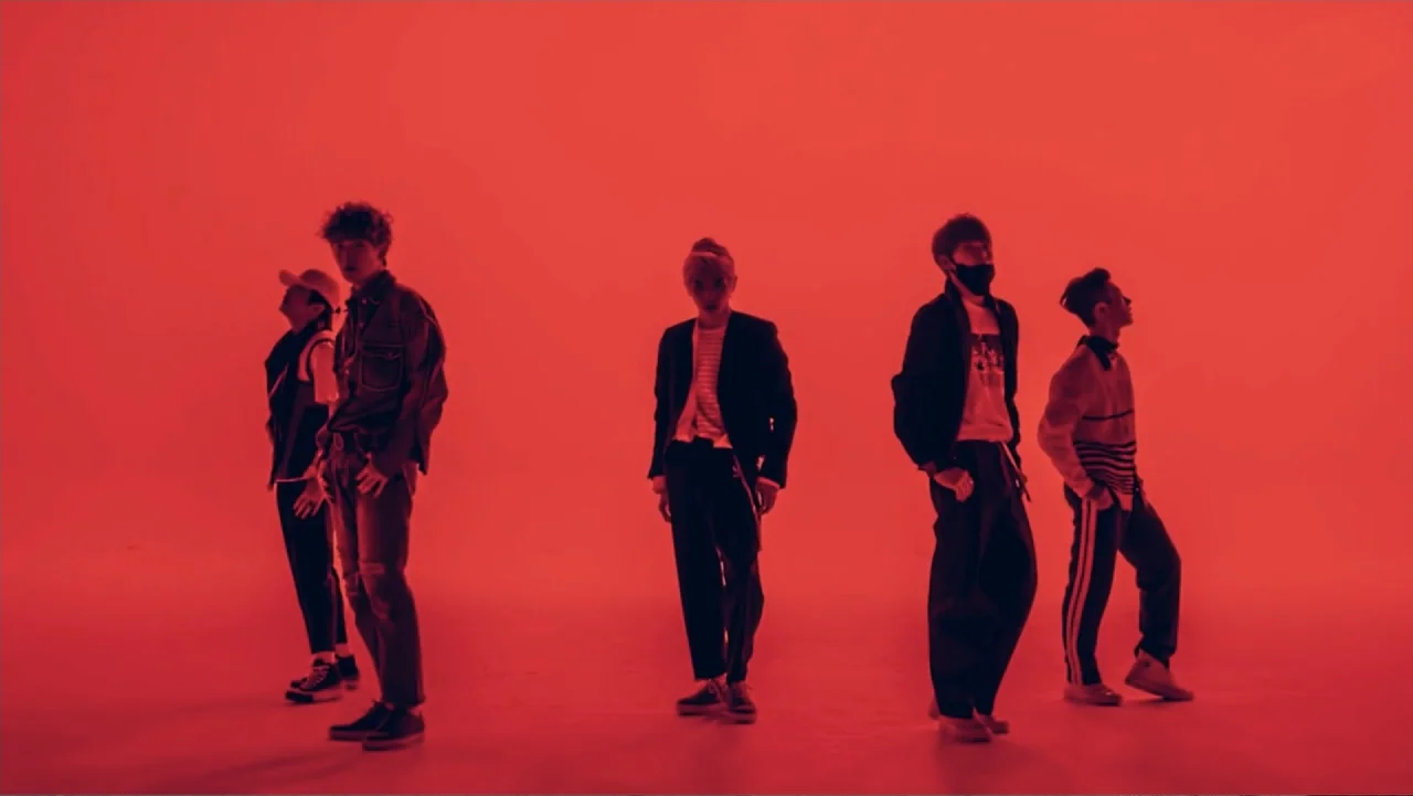 Lee Soo Man: King of K-Pop (2025) movie still: fullbody — A bare interior studio space with a solid red backdrop wall and floor. Five young men…