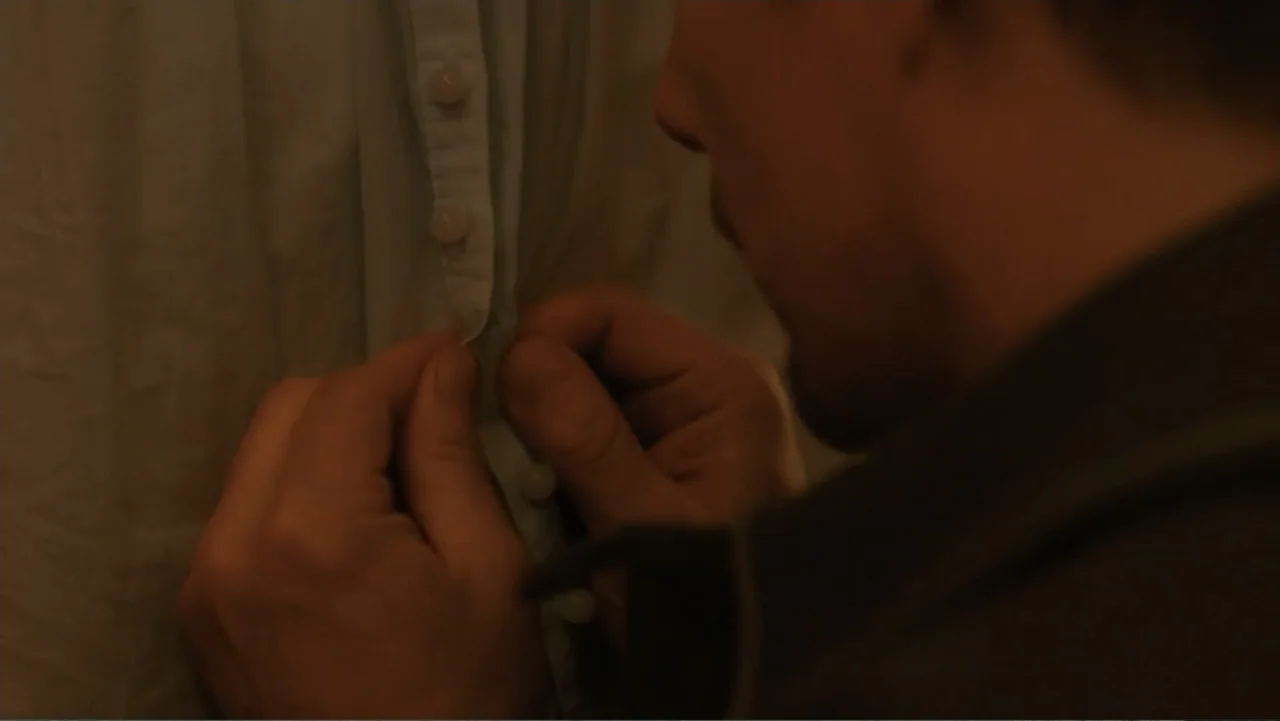 Maggie's Plan (2016) movie still: closeup — Close up on a person buttoning a light shirt. The framing is over the shoulder of the person doing the…