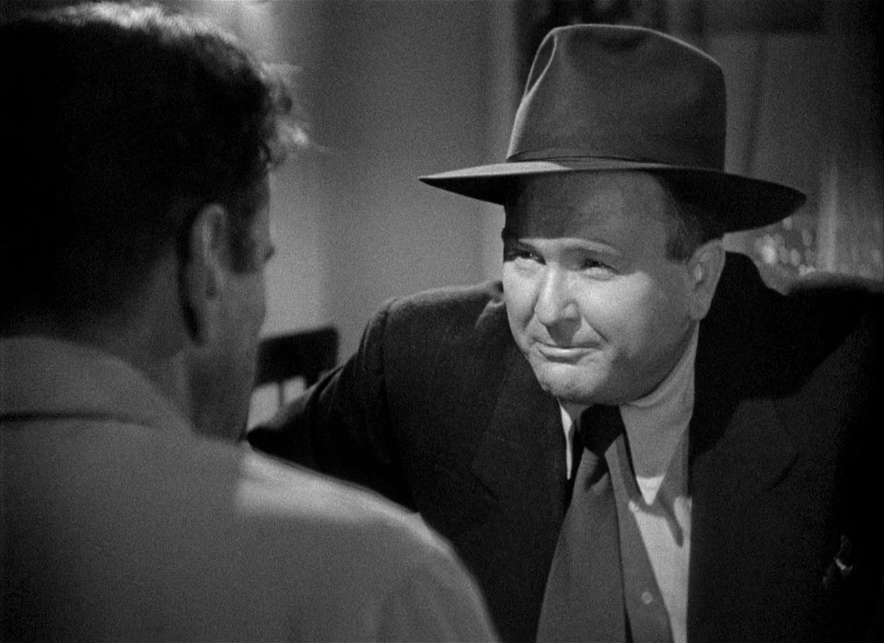 Dead Reckoning (1946) movie still: medium — A dark, dimly lit environment where two men engage in a private conversation. The foreground person is…