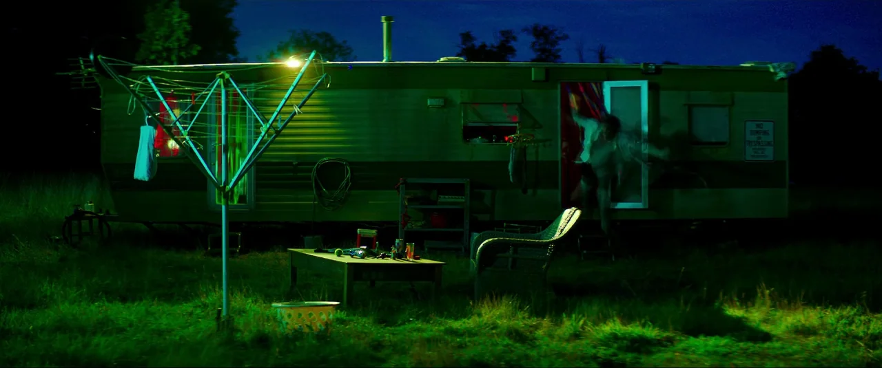 Mindhorn (2016) movie still: wide — A green mobile home sits in a dark field illuminated by an intense green light. An outdoor clothes drying rack…