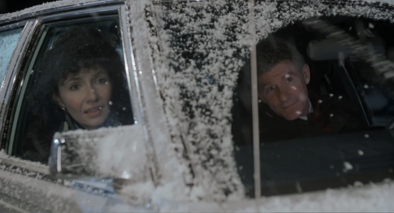 Dead of Winter (2025) movie still: medium — A dark car parked in a snowstorm features thick accumulations of snow on the exterior. An adult man and…