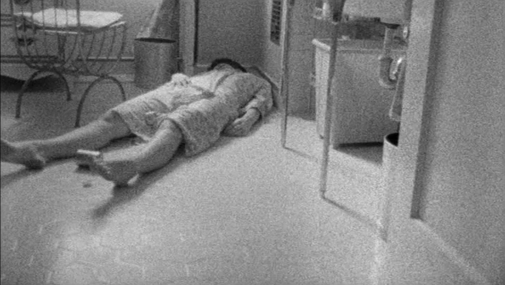Faces (1968) movie still: fullbody — A tiled room contains a small metal chair and a pedestal sink. A woman lies prone on the floor in her robe.