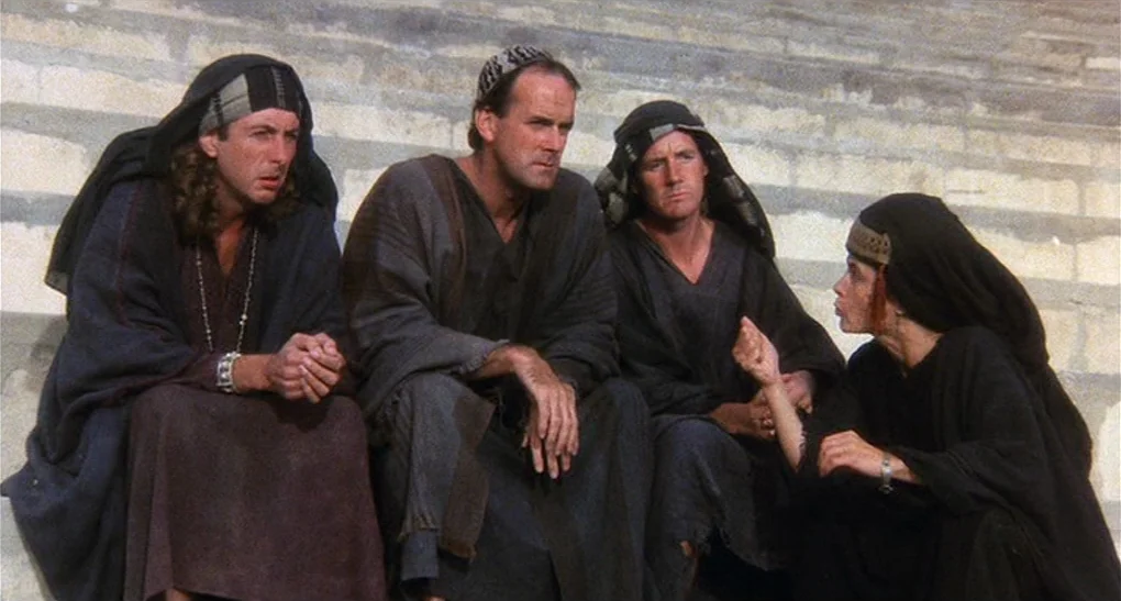 Life of Brian (1979) movie still: fullbody — A group of four people sit together on weathered light-colored stone steps. One woman gestures with her…