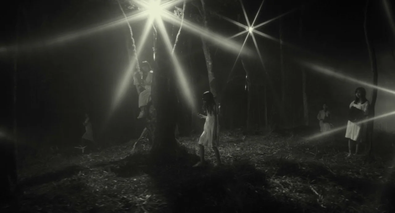 Making of: Antiporno (2016) movie still: wide — A dark, wooded area at night is illuminated by several intense, star-bursting spotlights. Multiple…
