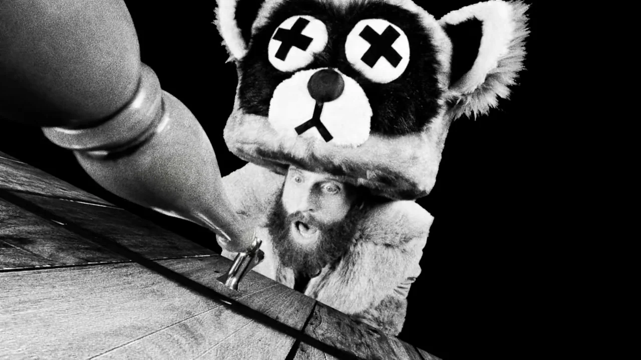 Hundreds of Beavers (2022) movie still: medium — A man in a furry raccoon costume stands behind a wooden bar counter. He is pulling down a metal tap…