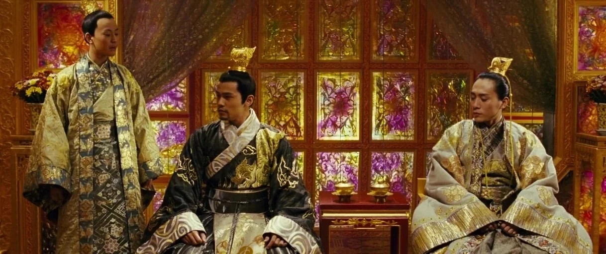 Curse of the Golden Flower (2006) movie still: fullbody — A palace room decorated with back-lit stained glass panels and gold wood paneling. Three…