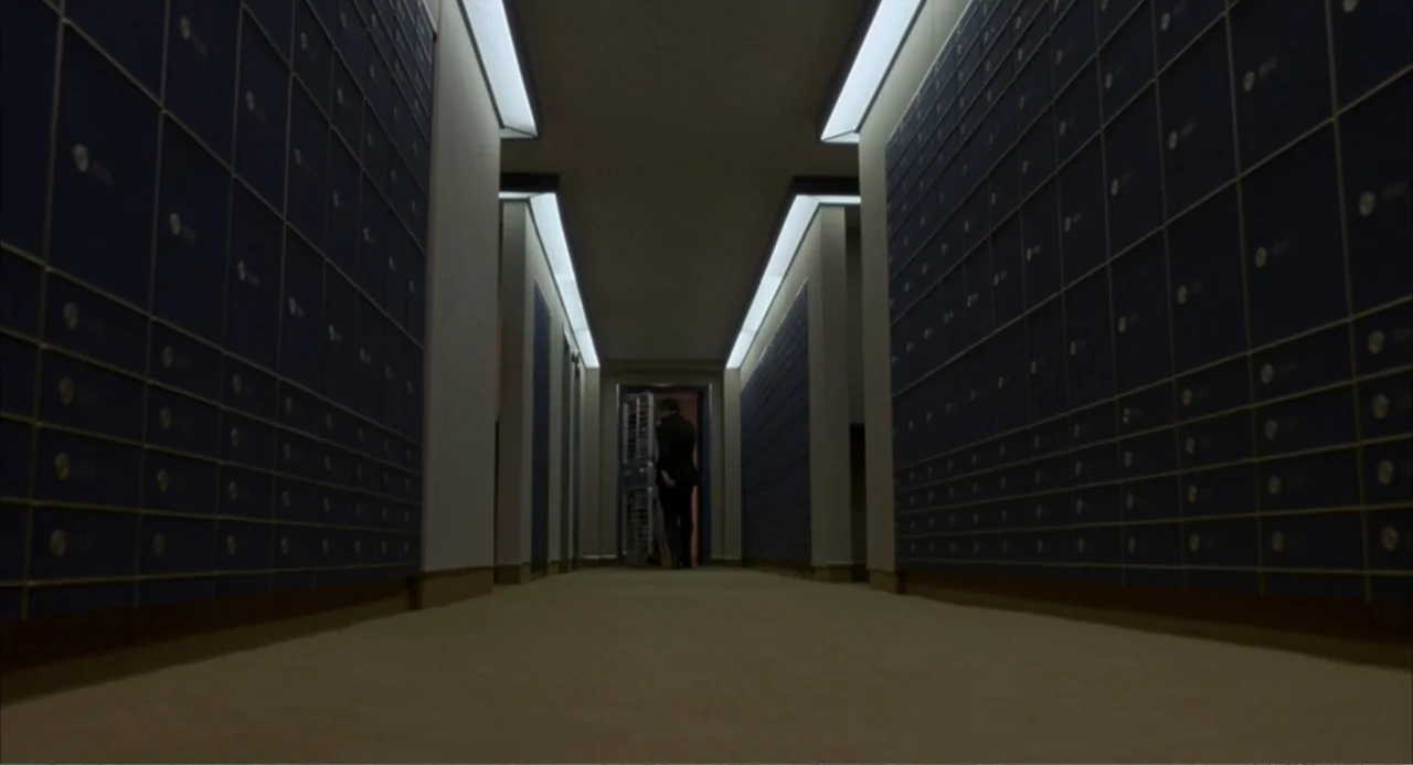 F/X (1986) movie still: wide — A long, symmetrical corridor lined on both sides with metal safe deposit boxes. A man in a dark suit walks away from…
