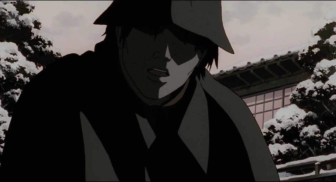 Millenium Actress (2001) movie still: closeup — A snowy courtyard with traditional Japanese architecture in the background. A man wears a dark coat…