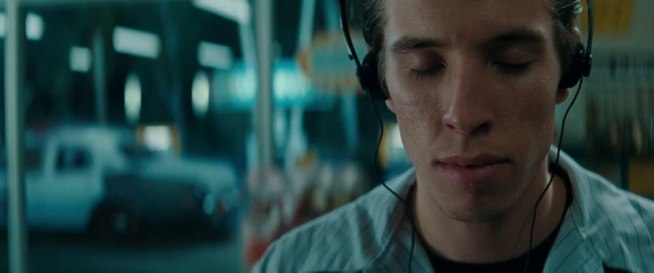 Super 8 (2011) movie still: closeup — A man wearing headphones stands at night in a location lit by glowing neon. He keeps his eyes closed while…