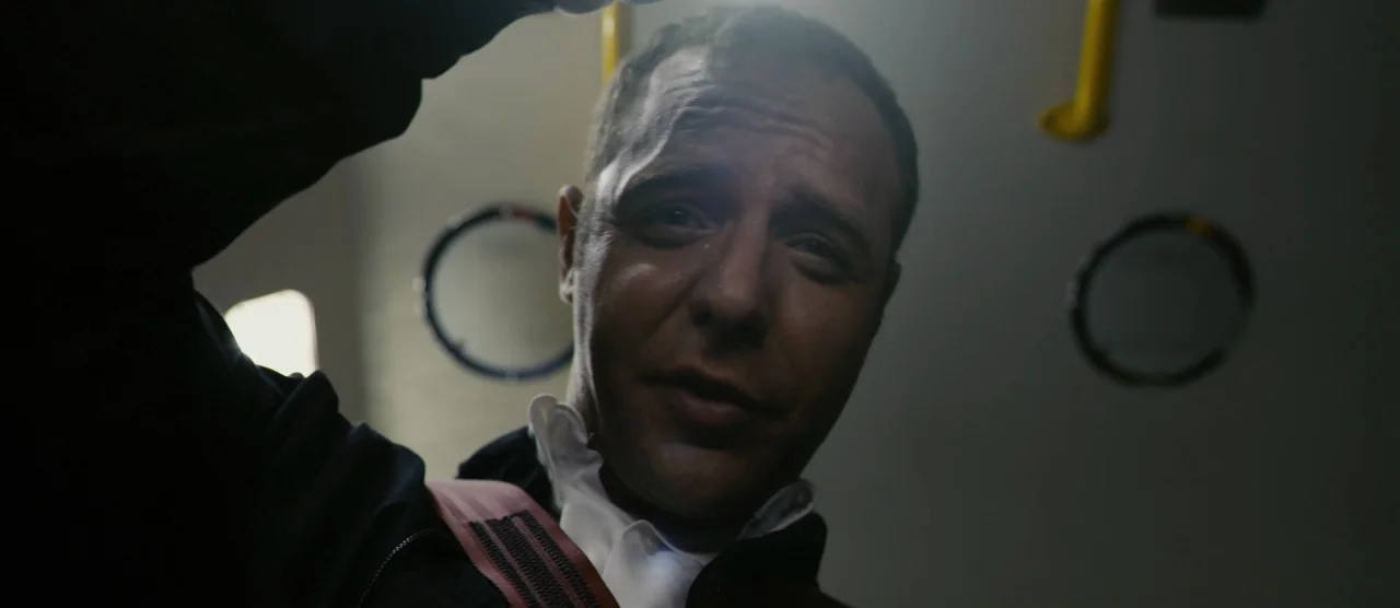 Self/less (2015) movie still: closeup — The interior of a commuter train car features yellow handrails and dark wall panels. A man in a dark jacket…